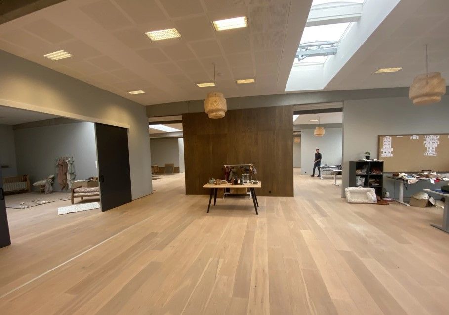 Rummelige kontorlokale med lyse trægulve og åbne lofter. Væggene er hvide og der er lysekroner og et skrivebord i midten af