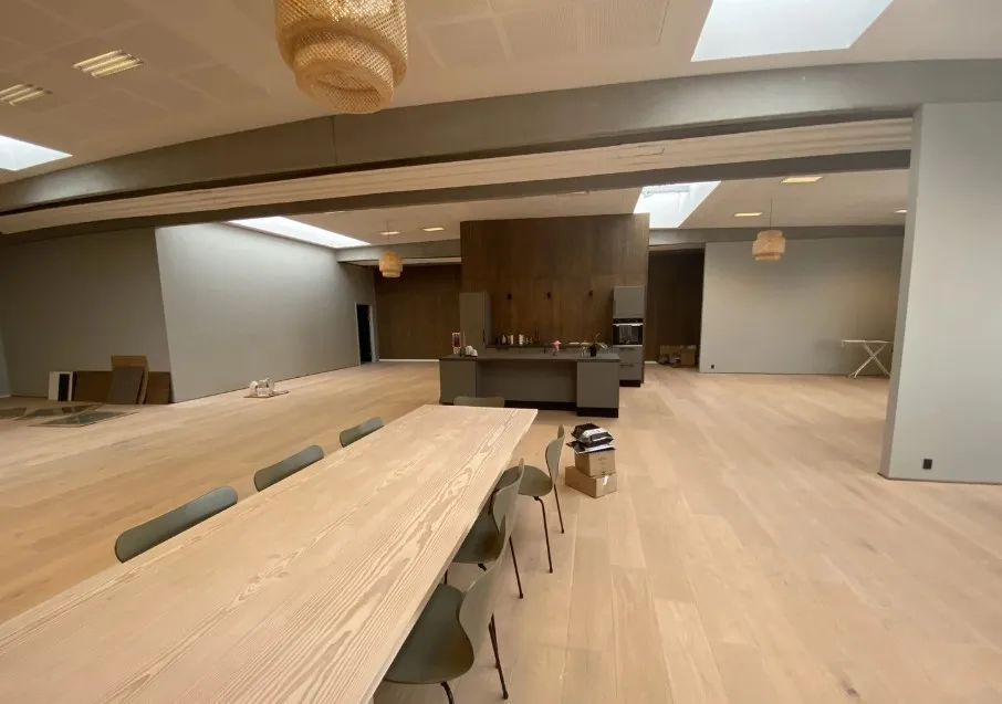 Rummeligt kontorlokale med moderne møbler og lyse lofter, der er i gang med renovering og indretning.