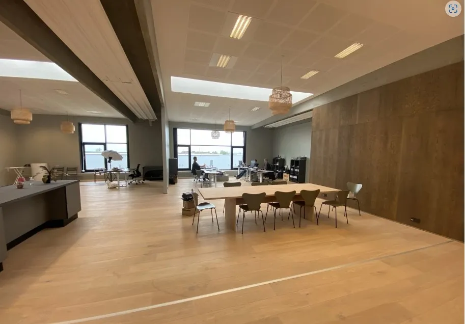 Moderne og rummeligt kontorlokale med lyse trægulve og høje lofter. Vinduesområder med udsigt til byen. Bord og stole står