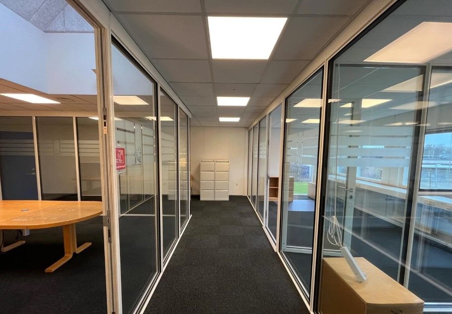 En tom kontorhal med glasvinduer og mørkegulv. En rund bord og et skab uden for vinduet.