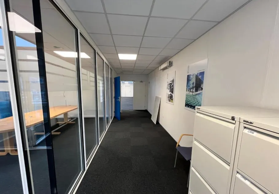 Lyst og moderne kontorlokale med glasvægge og møbler, træbord, kabinetter og hængede billeder