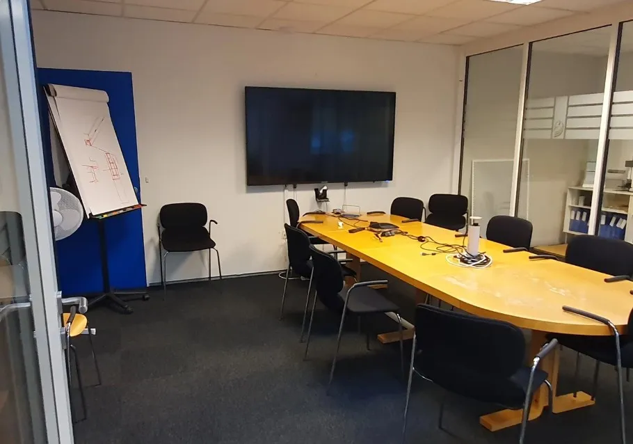 Kontorlokale med mødesal, skrivebord, stålstol og fladskærms-tv. Gulv og vægge er pænt og funktionelt indrettet