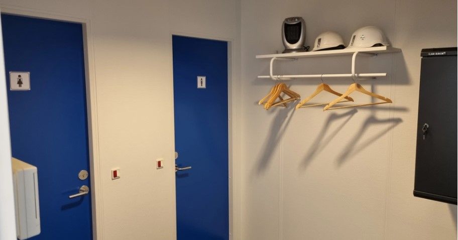 Køkkenområde med lyse blå døre, hvide vægge, hængehylde med hvidt stativ og lysebrune træhængere samt hjelme