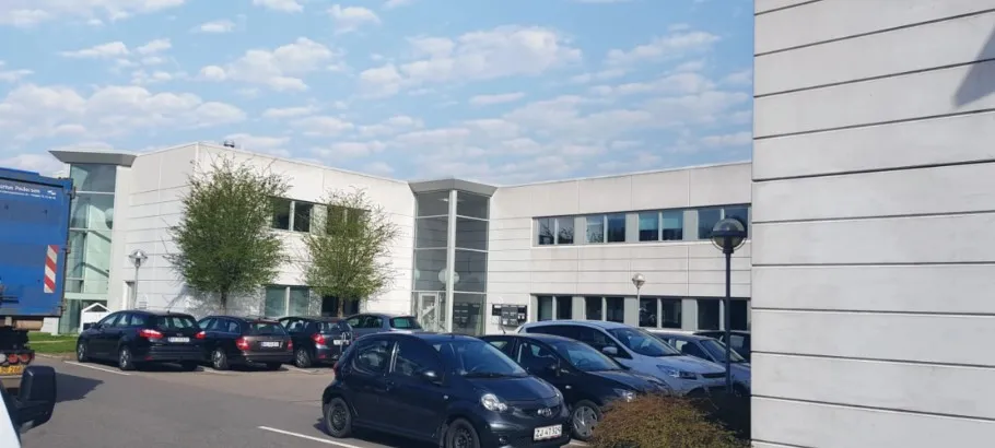 Mange biler parkeret foran Gunnar Clausens Vej 19A, og en stor bygning med mange vinduer og grønne træer