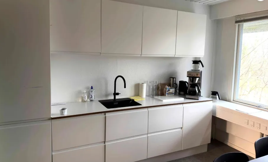 Rent køkken med hvide vægge, hvide skabsfronter og lysegule loftsbjælker. Sort vask med vandhane, kaffemaskine og skråbord