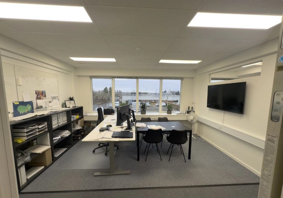 Kontor med bord, stol, computer, skrivebord, monitor og tv samt et skab med papir