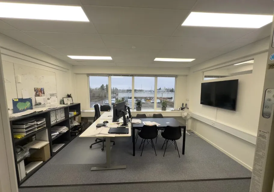 Kontor med bord, stol, computer, skrivebord, monitor og tv samt et skab med papir