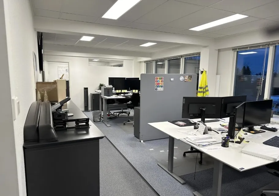 Et moderne kontor med lysegult gulv og hvide vægge, to store skriveborde og mange tekniske udstyr og stoffer