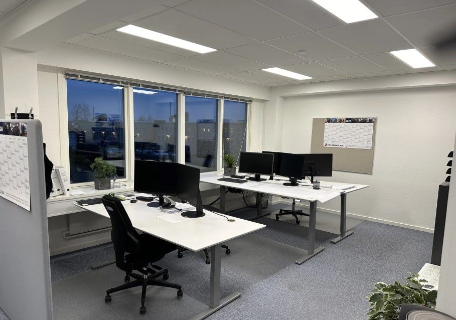 En moderne kontor med to bord, hver med flere skærme og en række planter