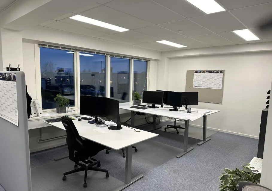 En moderne kontor med to bord, hver med flere skærme og en række planter