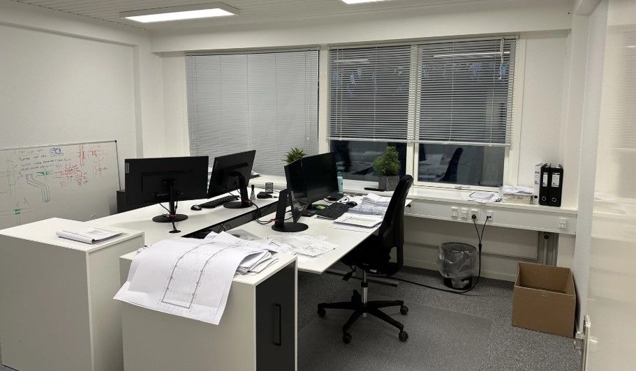 Et moderne kontor med lyse tavler og skriveborde med monitorer og planter. Række med bøjlebøger og skraldespand og smukke