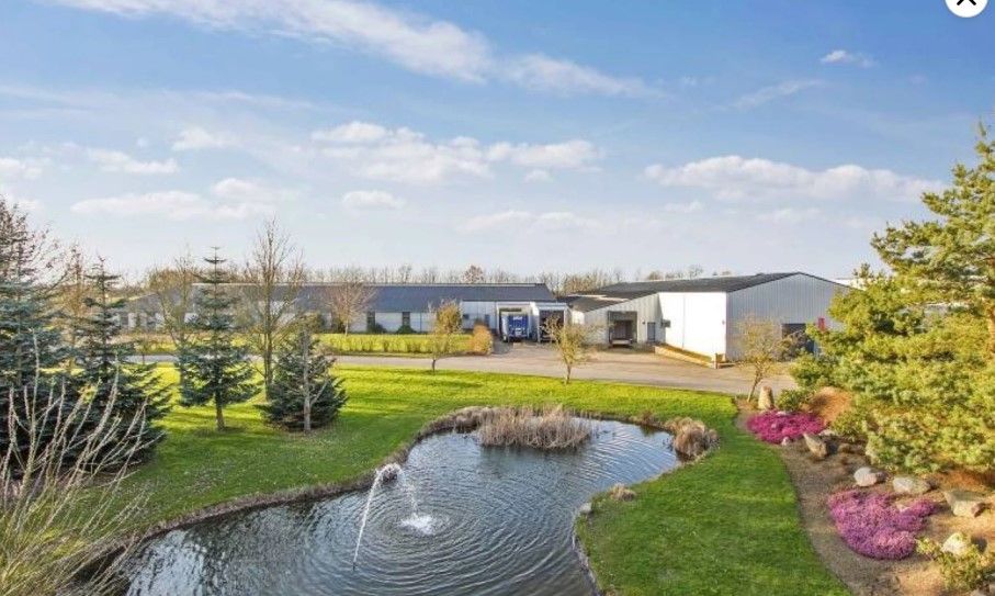 Fabrik med solceller på taget og vandhave med springvand foran i skovklædt område