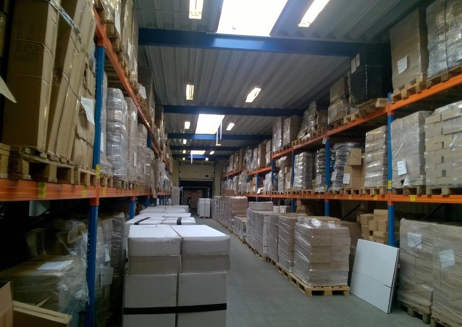 Lager med flere paller, kasser og emballagemateriale i en stor bygning med højloft
