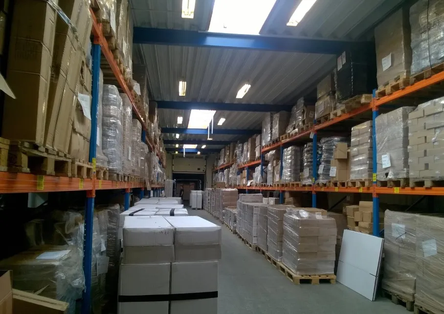 Lager med flere paller, kasser og emballagemateriale i en stor bygning med højloft