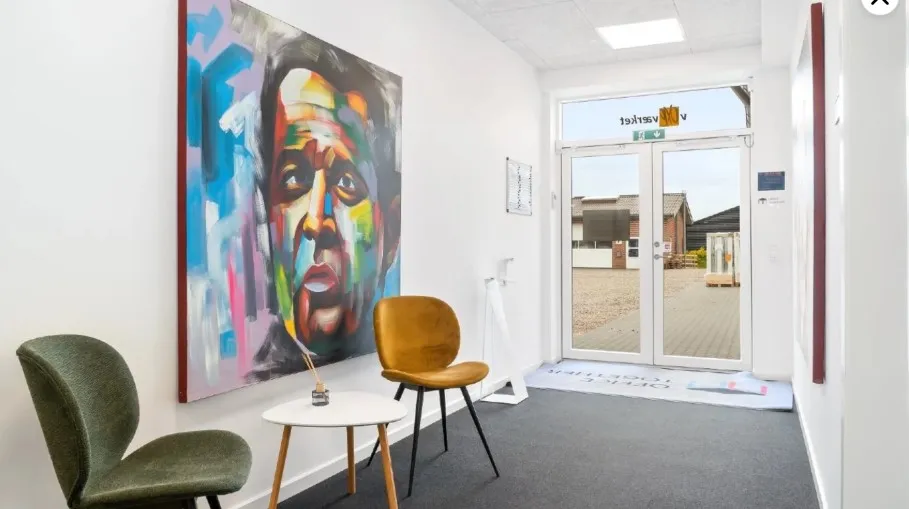 Kontorlokaler med moderne indretning og lyse farver, hvor der er en stor maleri, en gul stol og en grøn stol samt en lille