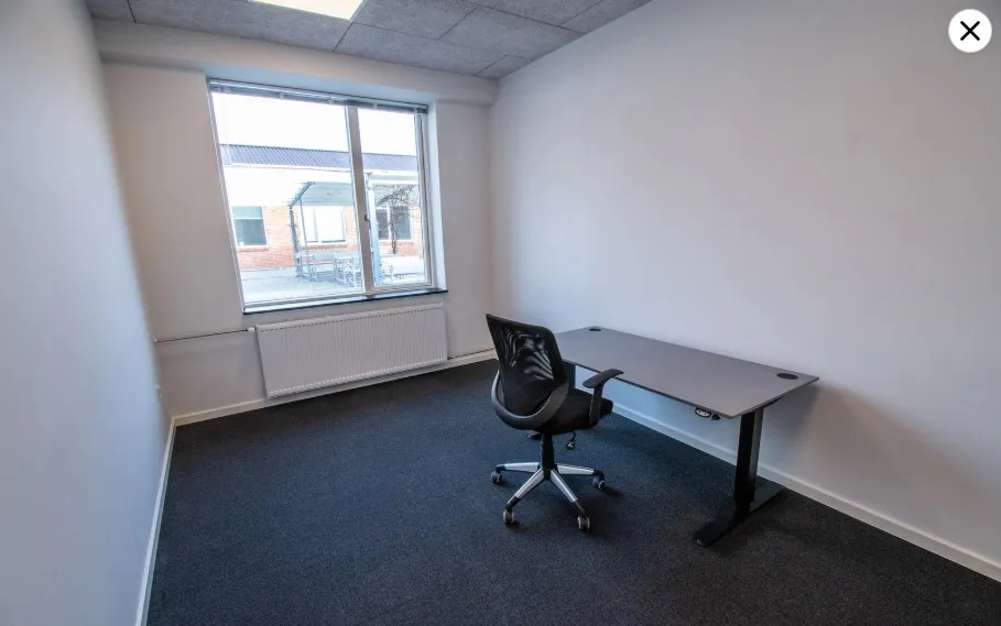 Et tomt kontor med lyse vægge, en høj radiator og et skrivebord med stol uden for kamerafeltet