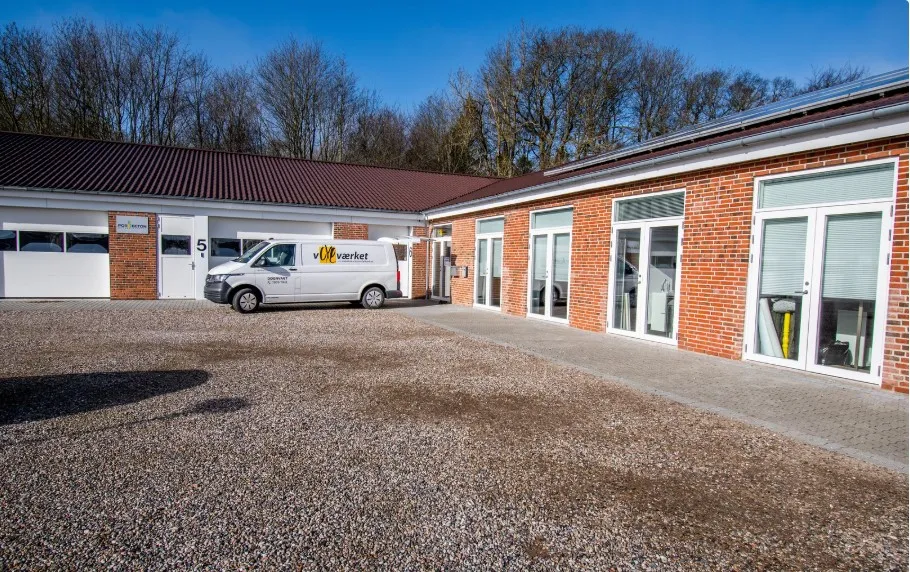 Kontorbyggeri med vinduer og solpaneler på taget, hvor en hvid Volkswagen transporter er parkeret foran