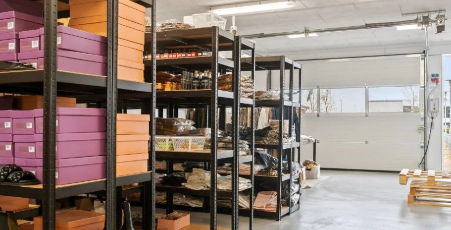 Lager med lagerhylder med bokse og kurve og udstyr lukket garagedør, vinduer, palet og lys i loftet