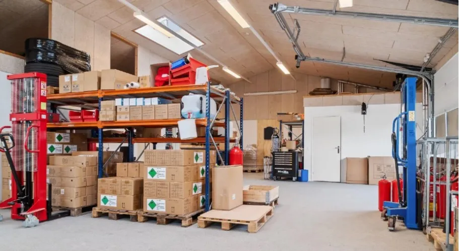 Lager med mange bokse og paller med forskelige varer og udstyr som slanger og brandslukkere.
