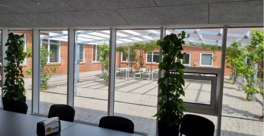 Kontor med store ruder og træstolpepergola, gulve med mursten og planter inde og udenfor.