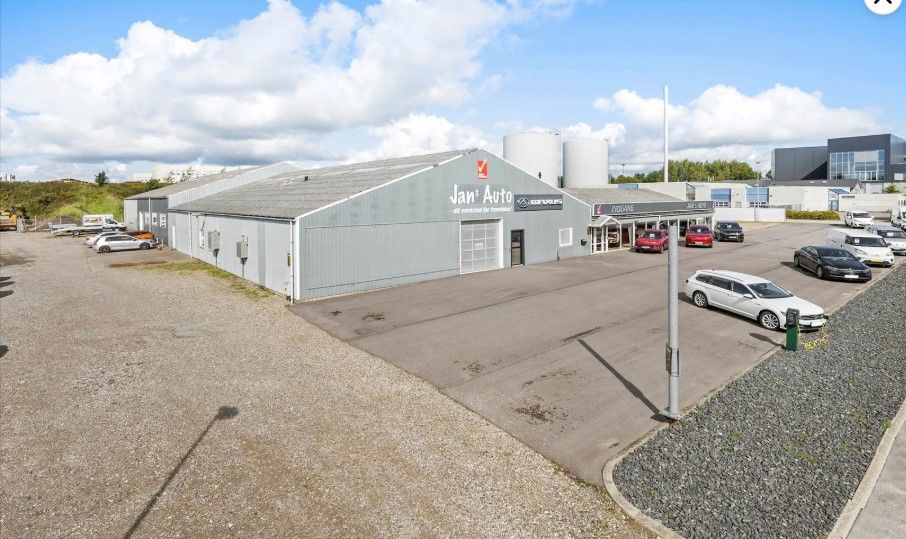 Et stort lagerhus med biler i parkeringspladsen og en stor skilt med Jan`s Auto på facaden