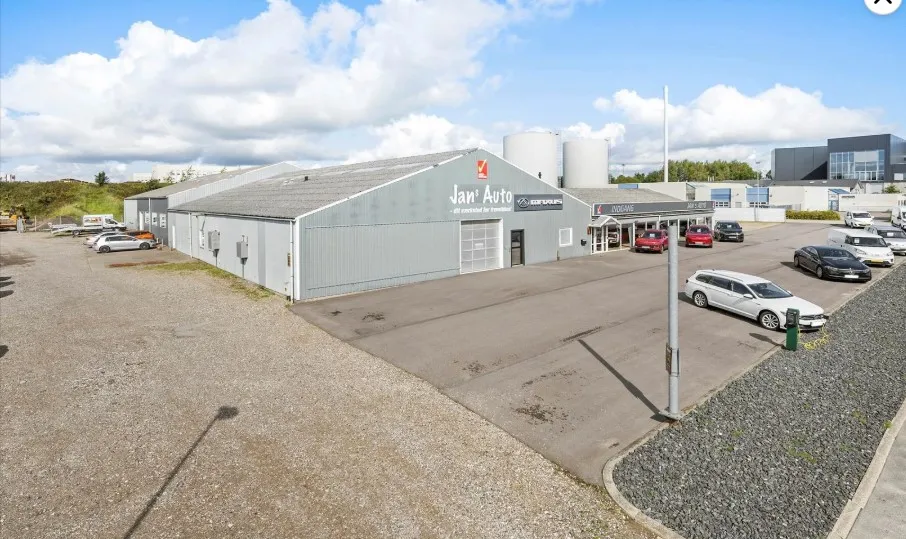 Et stort lagerhus med biler i parkeringspladsen og en stor skilt med Jan`s Auto på facaden