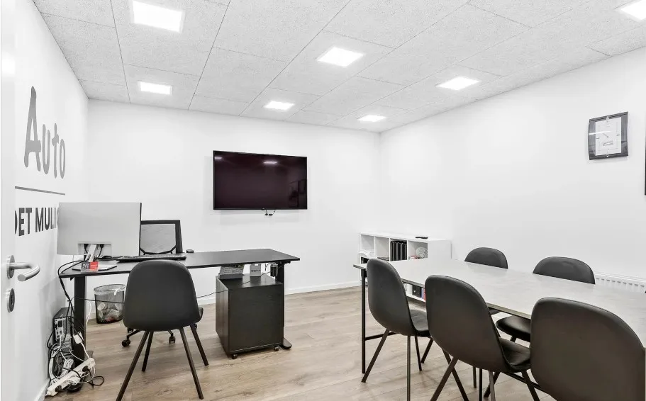 Kontor med to borde, computere og mødestoler med skrift på væggen og tv på væggen