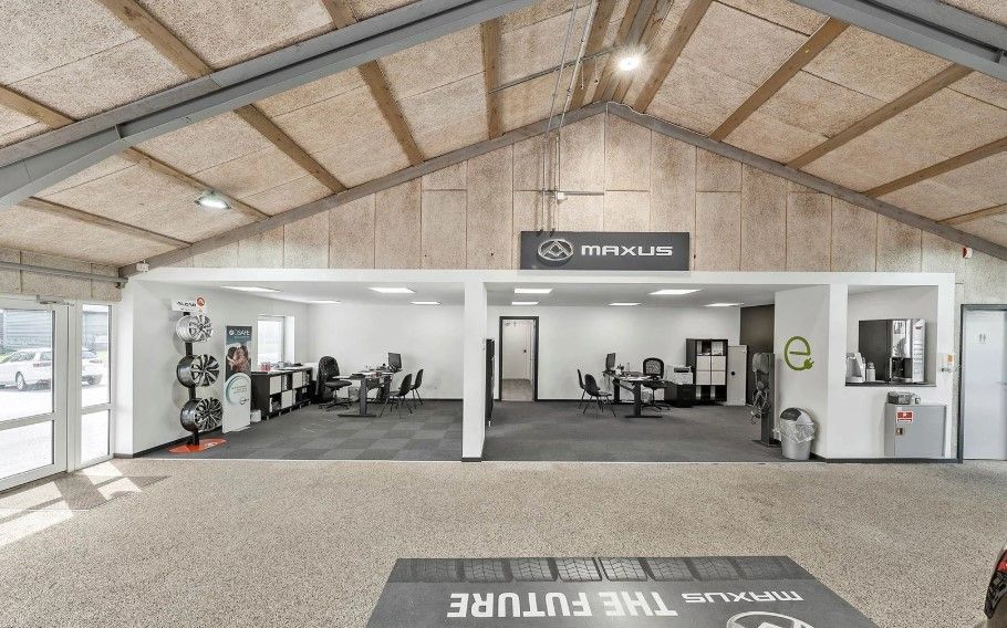 Forretningslokaler med et stort gulv og højt loft. En bordsætning med stole og en kaffemaskine er på gulvet.