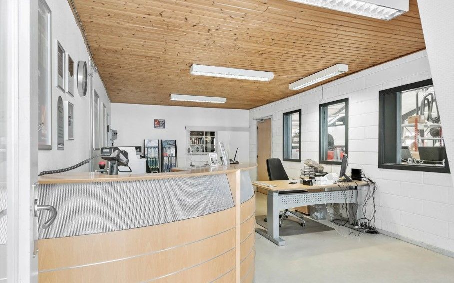 En møbleret industribygning med en stol, skrivebord og en kasseapparat, sammen med en modtager og flere billeder på væggen