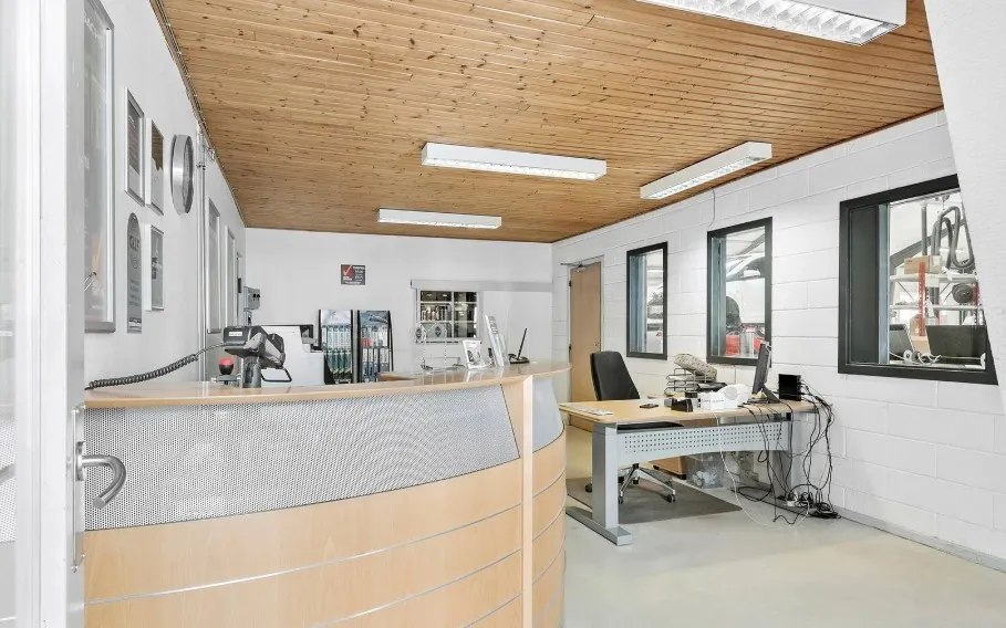 En møbleret industribygning med en stol, skrivebord og en kasseapparat, sammen med en modtager og flere billeder på væggen