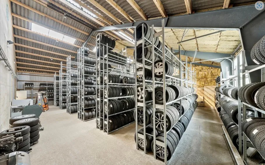 Lager med masser af dæk og hjul på store lagerhylder i en stor bygning med loft og vinduer