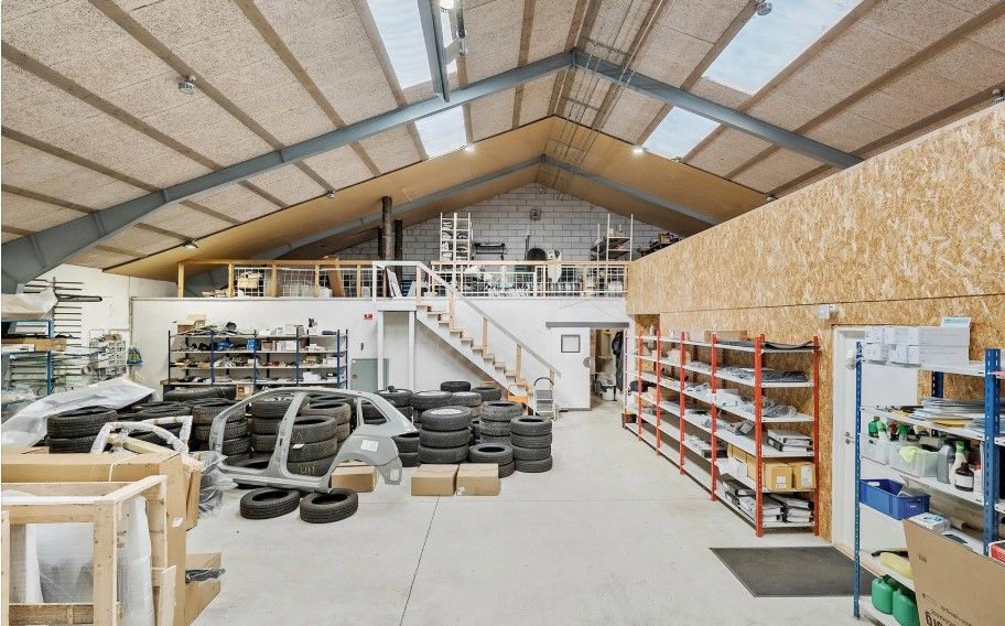 Industribygning med garage, lager og kontorlokaler i et rum, med trappe og vinduesparti, fuld af materialer og værktøj