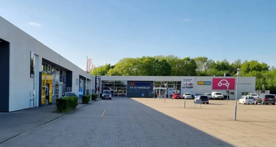 Butik med biler parkeret foran og flere biler parkeret i parkeringspladsen udenfor