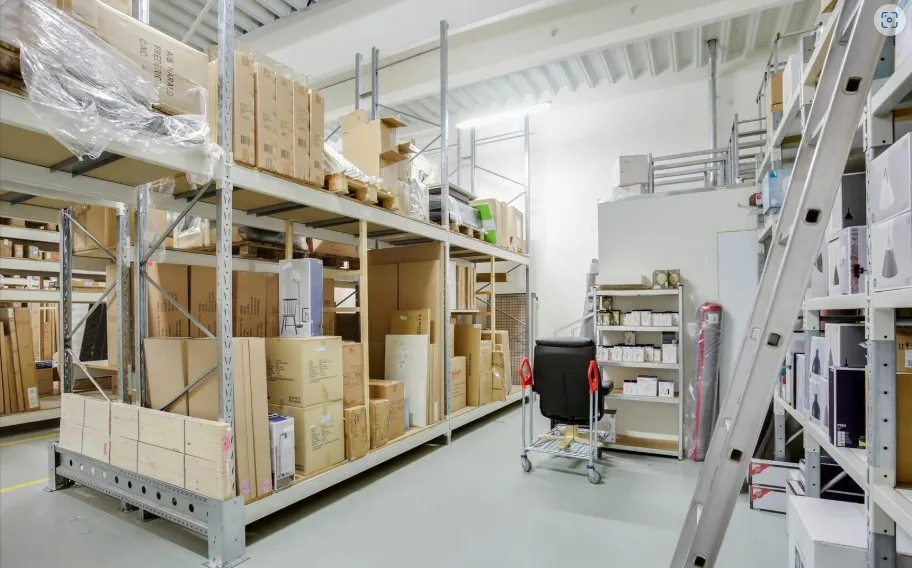 Lager med mange kasser og bokse samt metalreoler, kassevogn og stige