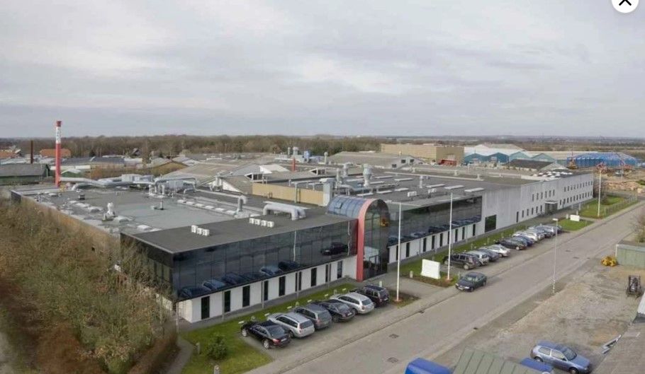 Fabrik med parkeringsplads for biler og udsigt over byggeplads og flere bygninger