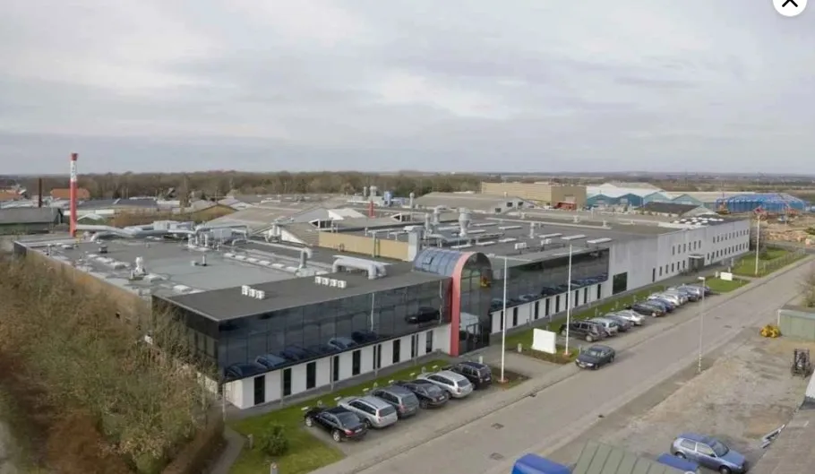 Fabrik med parkeringsplads for biler og udsigt over byggeplads og flere bygninger