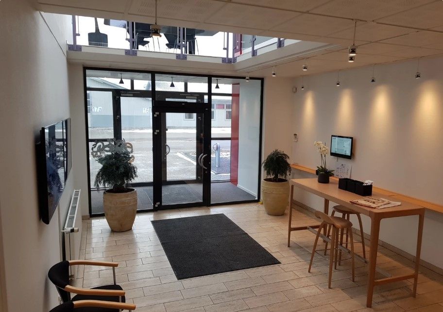 En kontorlobby med skrivebord, stole, en skraldespand og en tv-skærm. Der er en plante og et skrivebord med en skærm på det.