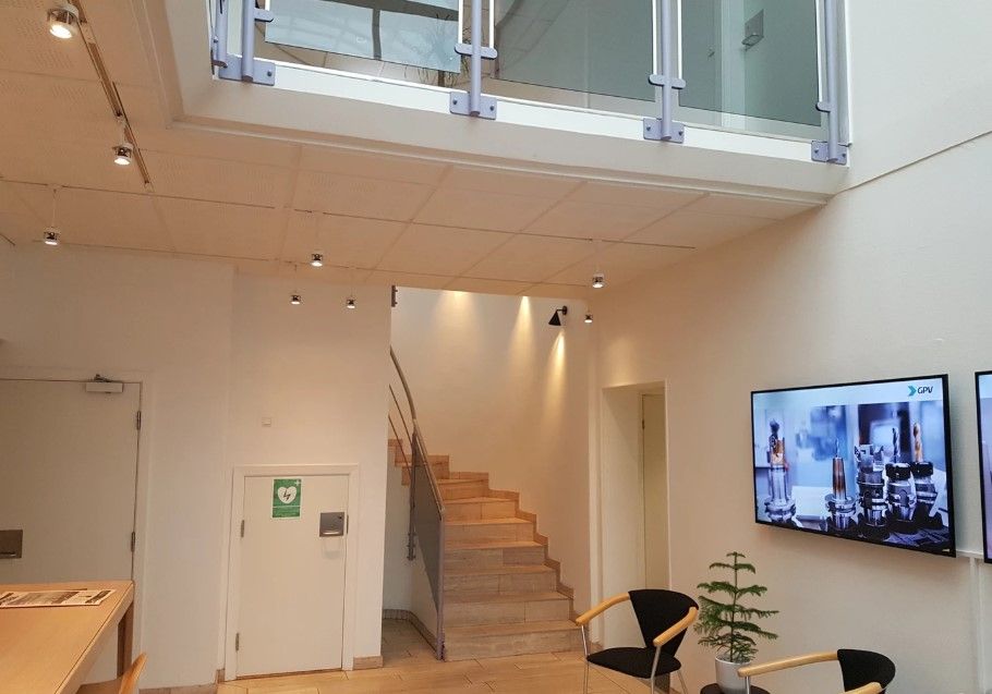 Inde i et kontorlokal er der to stole, en lille plante og en tv-skærm. Loftet er udstyret med flere lysekroner og et