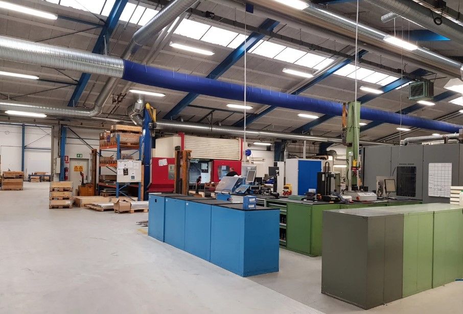 Fabrik med flere produktionsmaskiner og kontor. Høje lofter med store vinduer og lysekroner. Et stort lager med brædder og