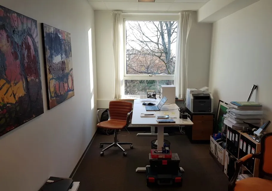 Kontor med lysegardiner og kunstværker, høj skrivebord, computer, stol og printer i Birkerød