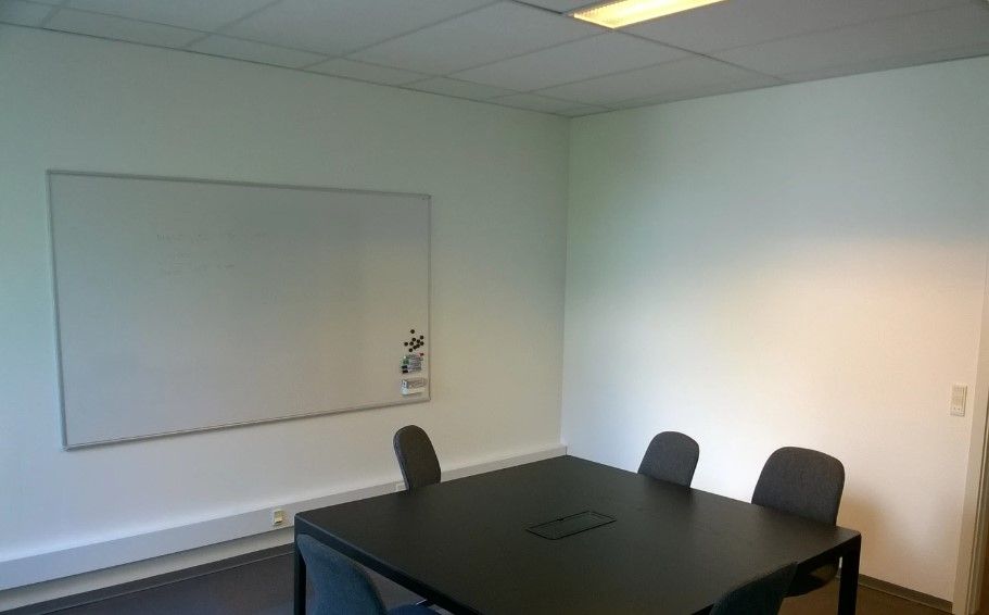 En tom kontor med mørke bord og stole samt et stort whiteboard med nogle stifter og en stikkontakt