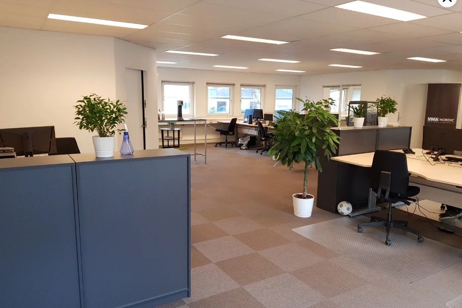 Kontor med lyse loftslampe, gulvbelægning, flere skriveborde og stole, spiselige plante i hvidt potter og flere stol