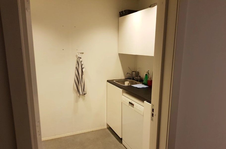 Køkken med hvide vægge og højloft, køkken med hvidt skab, sort bordplade, lysegrå gulv og hængende håndklæde