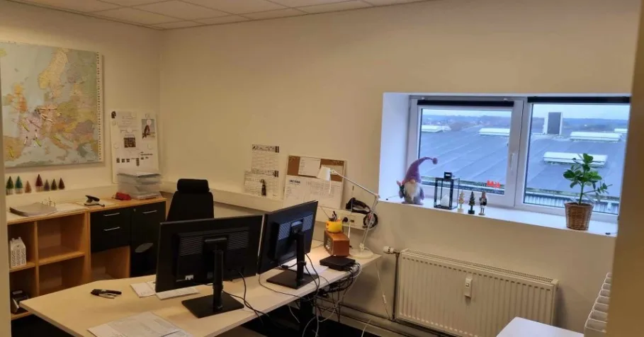 Et kontor med et bord med to computere, en plante og et hvidt radiator.