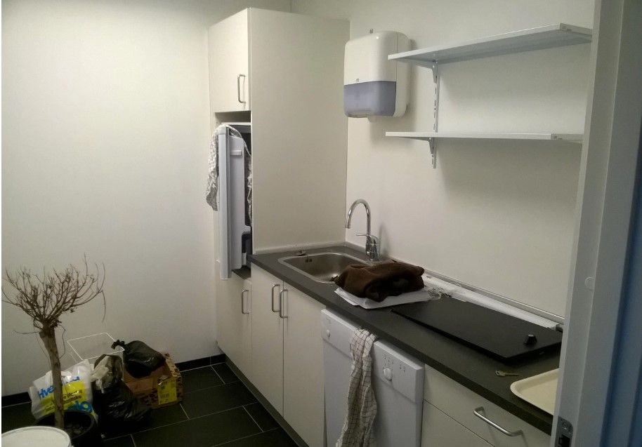 Kontorlokale med køkken, hvidt køleskab, vaskemaskine, køkkenhylder og håndklæder.