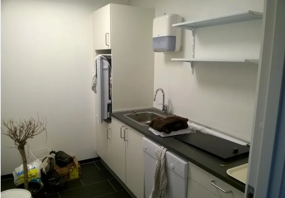 Kontorlokale med køkken, hvidt køleskab, vaskemaskine, køkkenhylder og håndklæder.