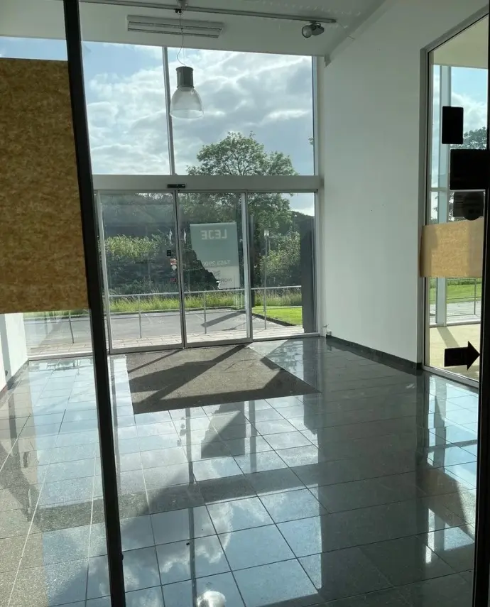 Et stort tomt rum med glasdøre og vinduer, en lys plet på gulvet og en skygge af et lys.