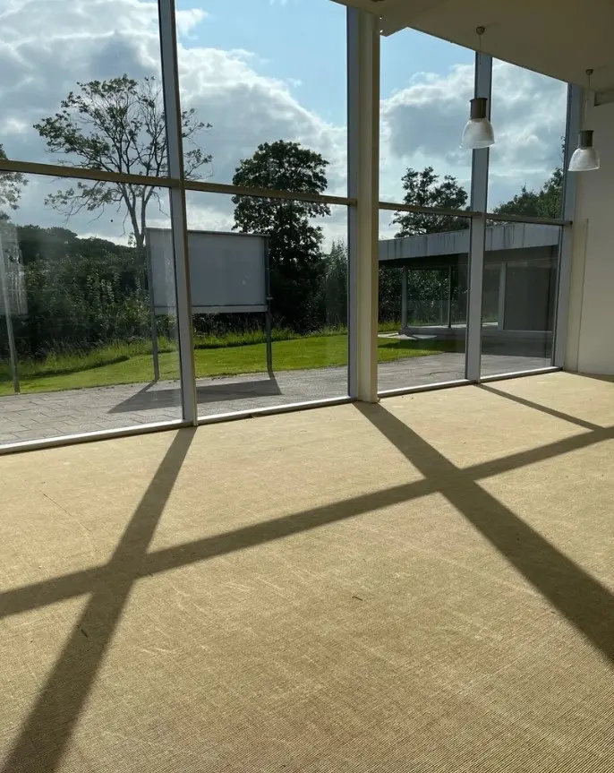 En stor lys stue med trægulv og glasvinduer med udsigt til en græsplæne og et træ med skyer på himlen