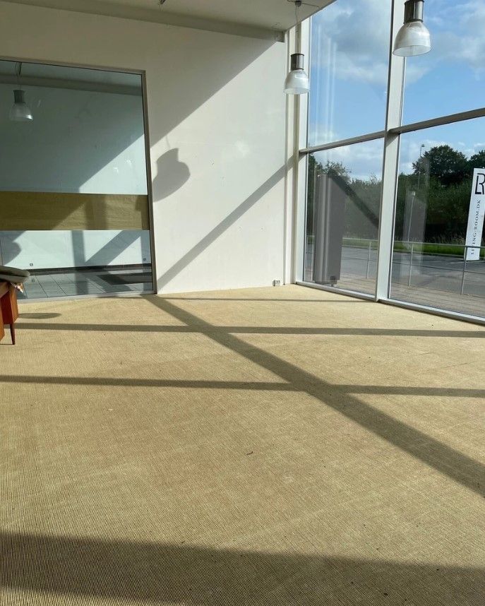 En stor, tom og lys stue med højloft og gulvbelægning i brunt og beige, der reflekterer sollyset