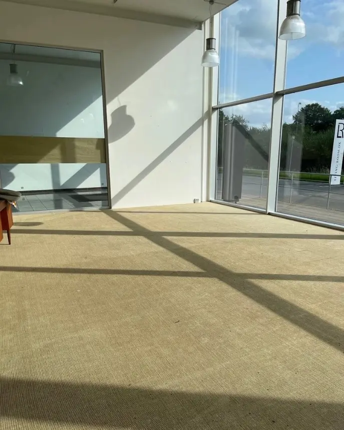 En stor, tom og lys stue med højloft og gulvbelægning i brunt og beige, der reflekterer sollyset